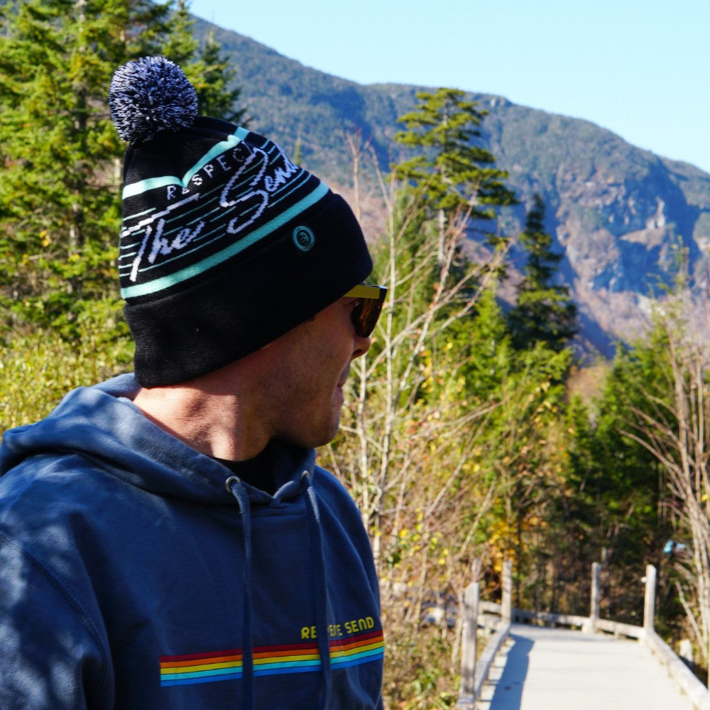 Jerry of the Day Respect the Send VHS Sweatshirt in blue and Respect the Send Vice Beanie in black and teal, man on mountain hike. Funny ski and snowboard gifts, shirts and apparel.
