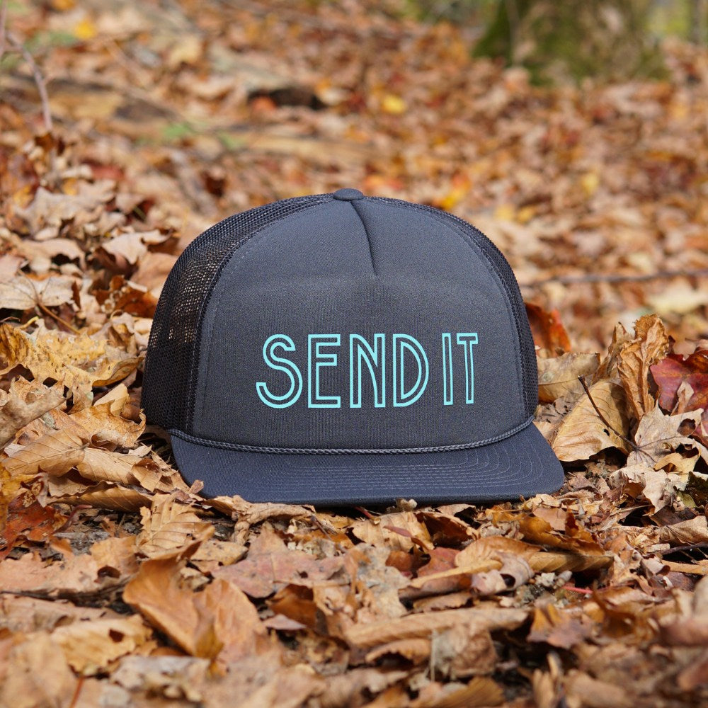 Jerry of the Day Send It Trucker Hat in navy, outside sitting in leaves. Funny ski and snowboard gifts, shirts and apparel.